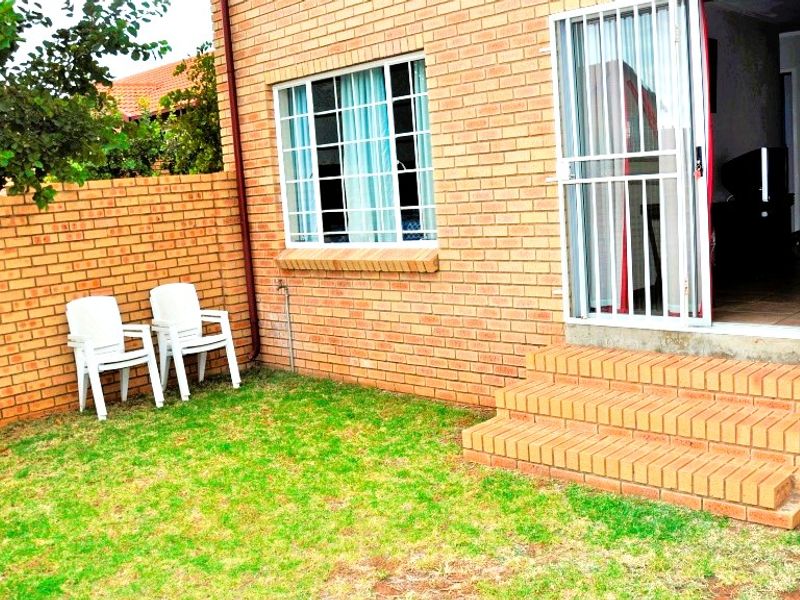Rear exterior view of the townhouse featuring face brick walls, a security gate entrance, and brick steps leading into the home.