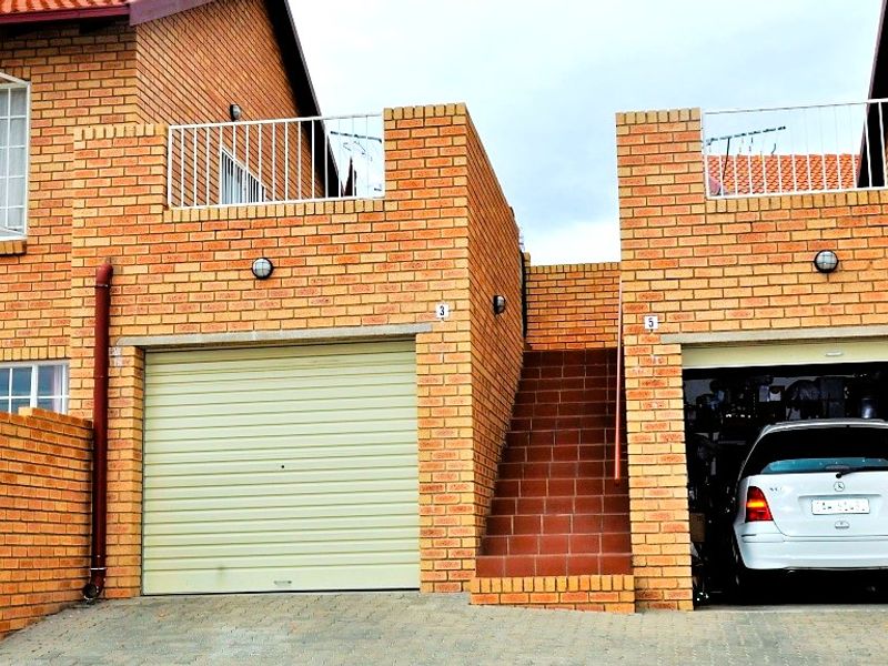 Front elevation of a face brick townhouse complex featuring two garage units, an external staircase, and upper-level balcony railings.