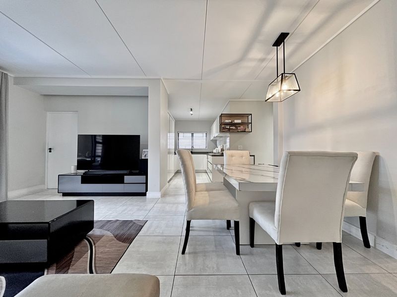 Modern open-plan living and dining area featuring neutral tiled flooring, contemporary pendant lighting, and a sleek, well-maintained kitchen with ample cabinetry.