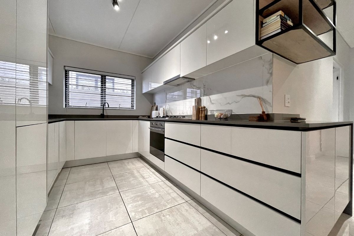 Modern kitchen featuring high-gloss white cabinetry, stone countertops, marble-look splashback, integrated oven, and sleek tiled flooring.