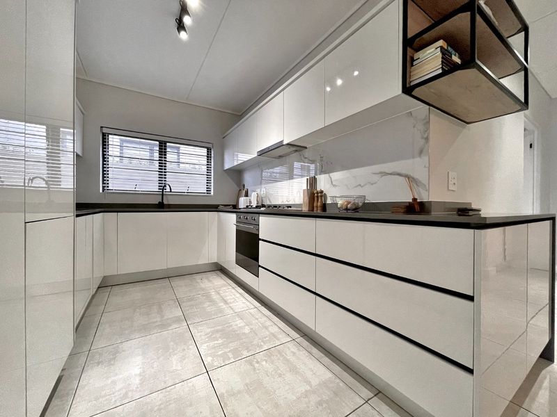 Modern kitchen featuring high-gloss white cabinetry, stone countertops, marble-look splashback, integrated oven, and sleek tiled flooring.