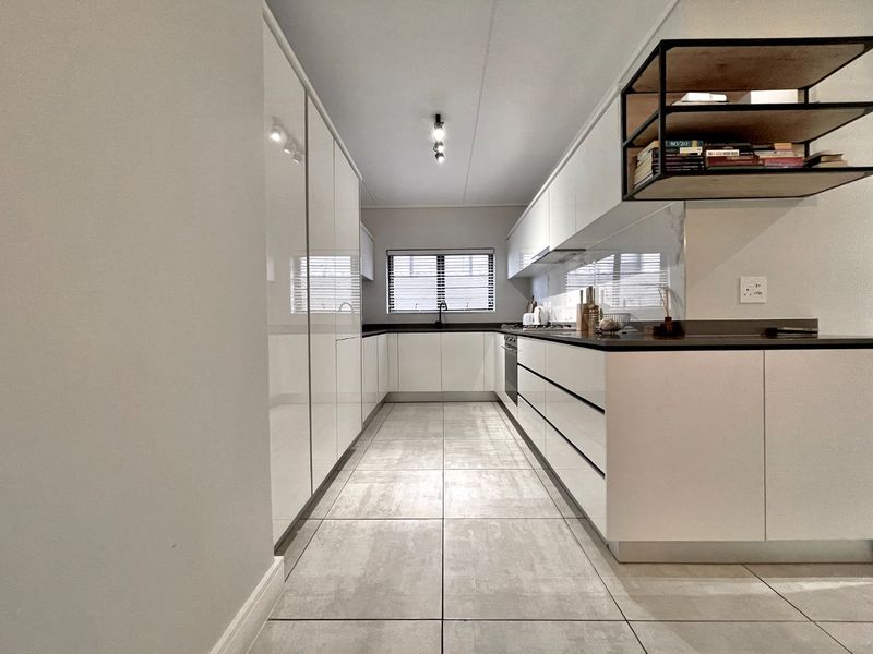 Modern galley-style kitchen featuring high-gloss white cabinetry, dark stone countertops, integrated appliances, and sleek tiled flooring.
