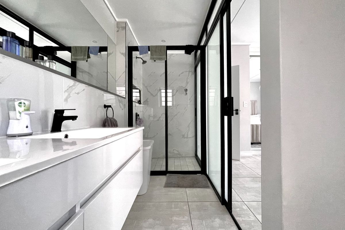 Modern bathroom featuring a floating vanity with integrated basin, black matte fixtures, and a spacious walk-in shower with marble-look tiling and black framed glass.