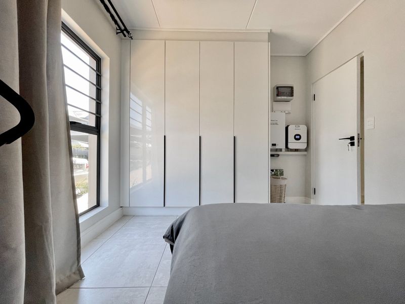 Modern bedroom featuring sleek white built-in cupboards, tiled flooring, and an integrated inverter system for power backup.