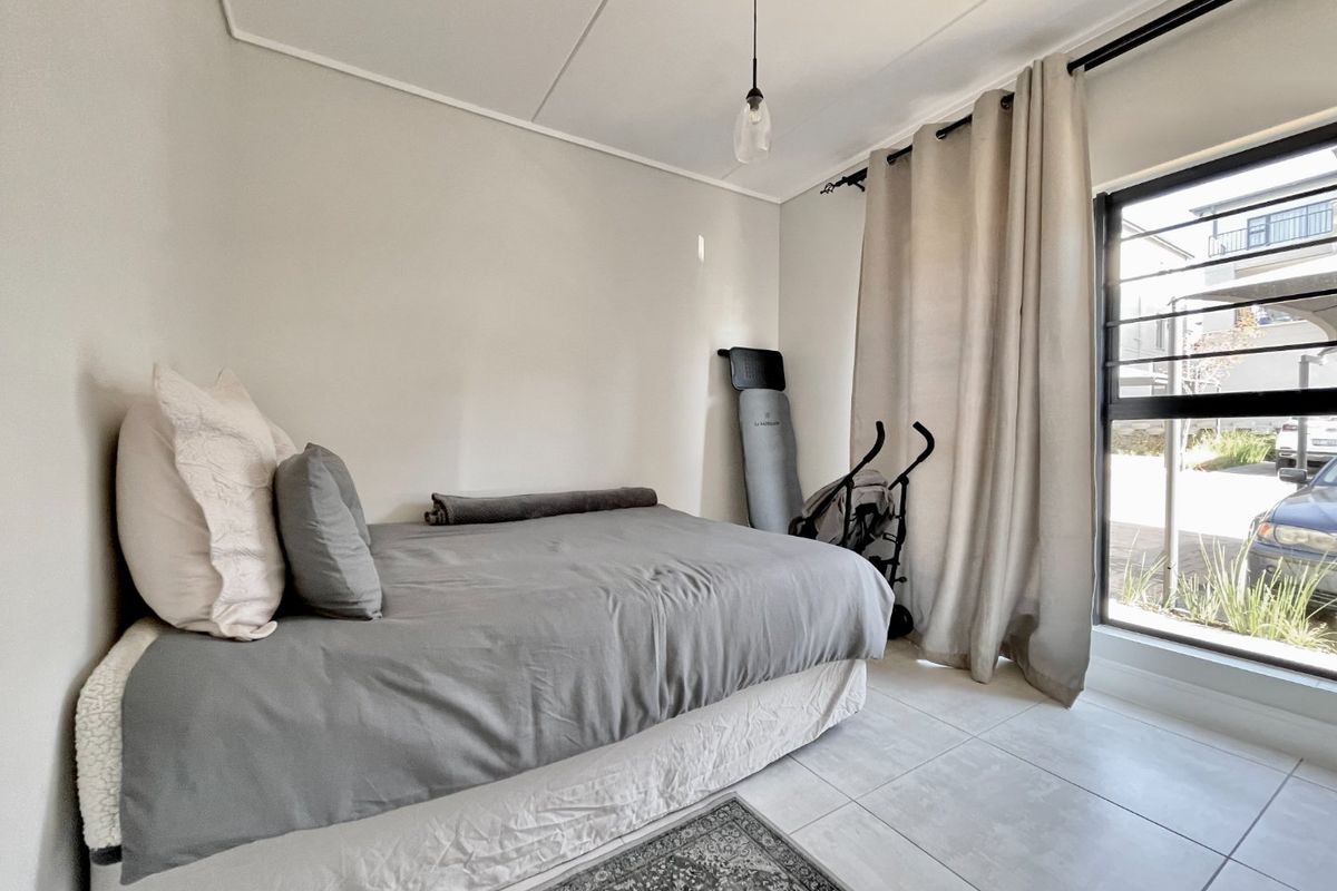 A bright bedroom featuring neutral walls, large window with curtain rails, and tiled flooring, offering a clean and functional living space.