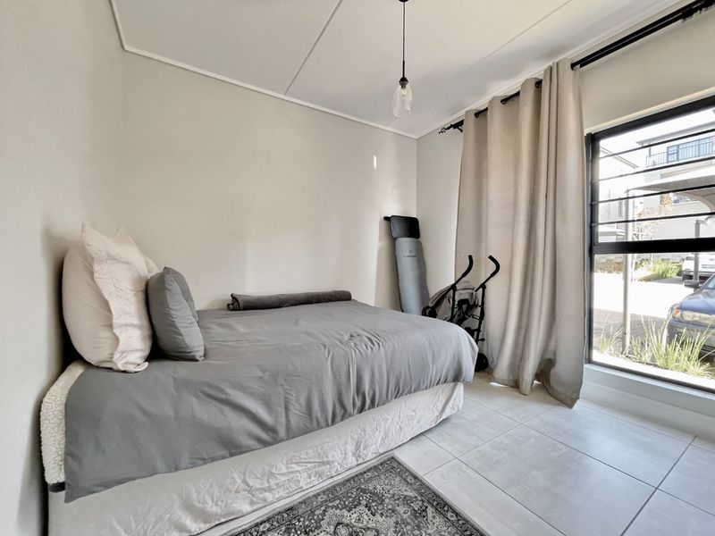 A bright bedroom featuring neutral walls, large window with curtain rails, and tiled flooring, offering a clean and functional living space.