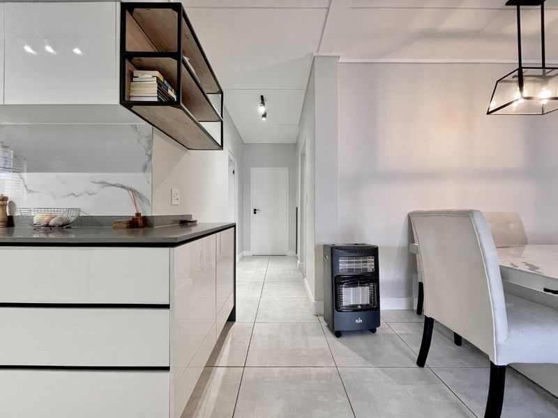 Modern open-plan kitchen and dining area featuring sleek high-gloss cabinetry, stone countertops, marble-look splashback, and contemporary tiled flooring throughout.