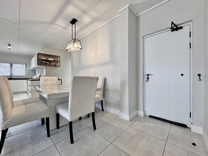 An open-plan dining and kitchen area featuring neutral tiled flooring, modern pendant lighting, and clean white finishes throughout.
