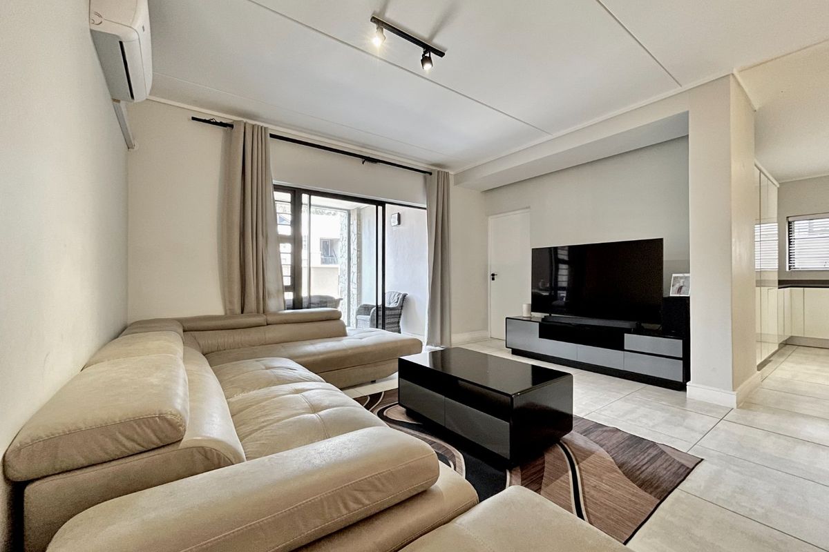 A well-maintained living room featuring tiled flooring, track lighting, and a split-system air conditioner, with direct access to an outdoor patio area.