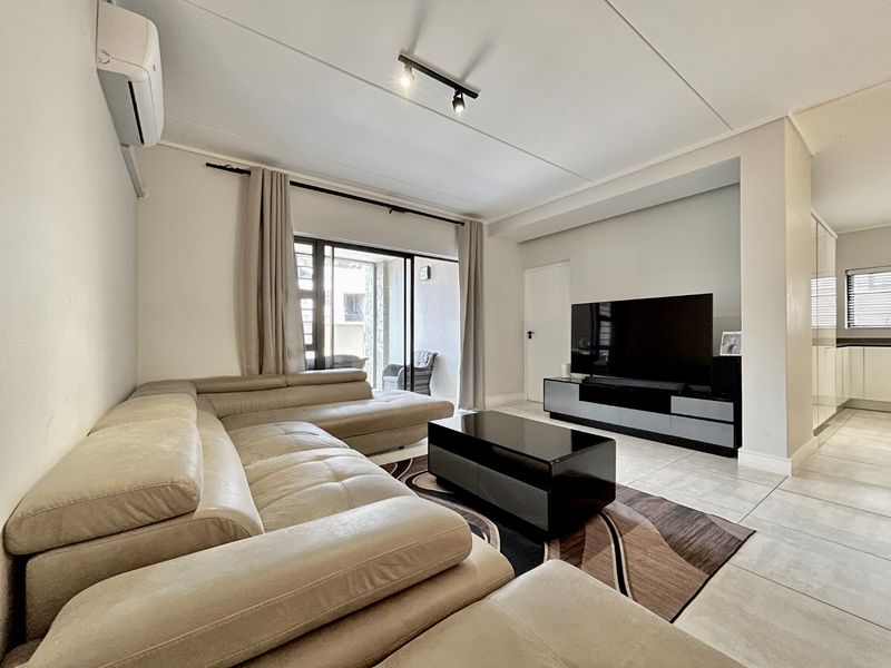 A well-maintained living room featuring tiled flooring, track lighting, and a split-system air conditioner, with direct access to an outdoor patio area.