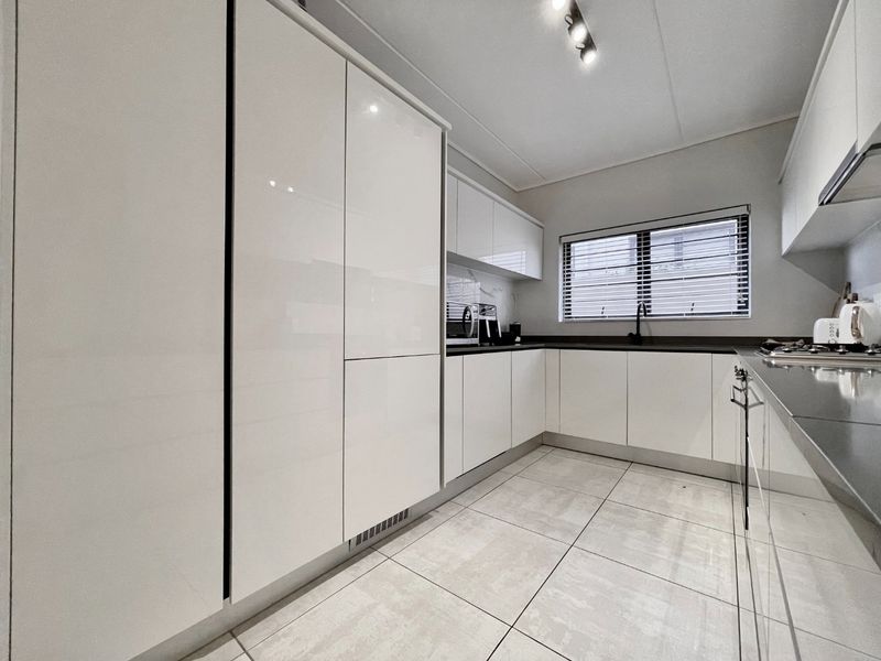 Modern kitchen featuring sleek white high-gloss cabinetry, dark stone countertops, integrated appliances, and contemporary tiled flooring.