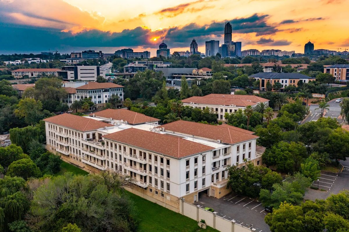 Aerial view of a multi-story commercial office building featuring a terracotta tile roof, surrounding landscaped grounds, and dedicated paved parking facilities.