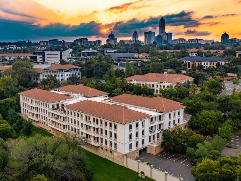 Aerial view of a multi-story commercial office building featuring a terracotta tile roof, surrounding landscaped grounds, and dedicated paved parking facilities.