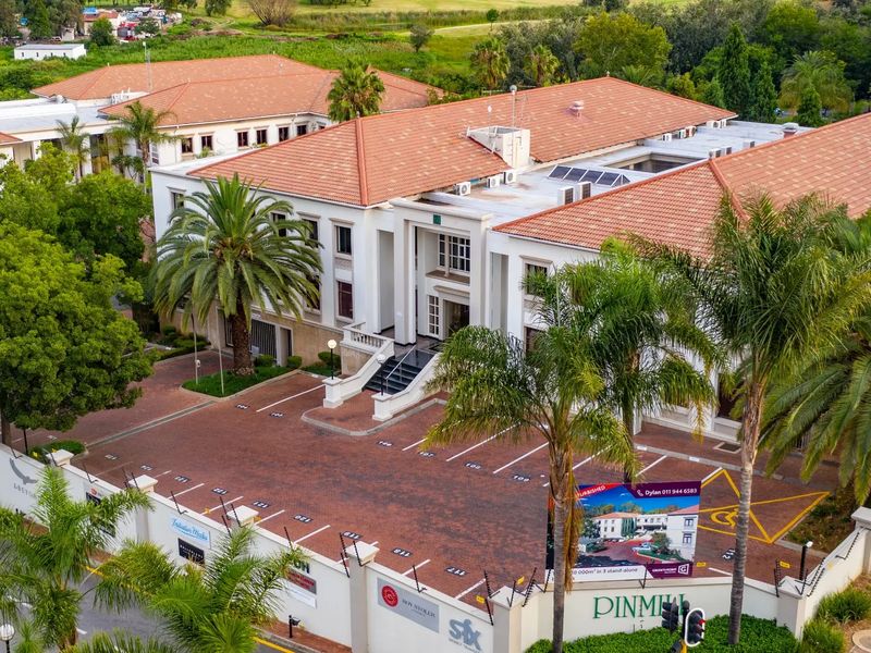 Aerial view of a commercial office complex featuring a terracotta tiled roof, paved parking area, and secure perimeter fencing.