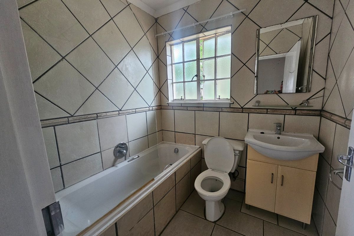 A dated bathroom featuring a built-in bathtub, toilet, and vanity cabinet with a washbasin, finished with full-height wall tiling.