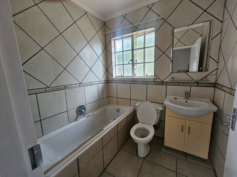 A dated bathroom featuring a built-in bathtub, toilet, and vanity cabinet with a washbasin, finished with full-height wall tiling.