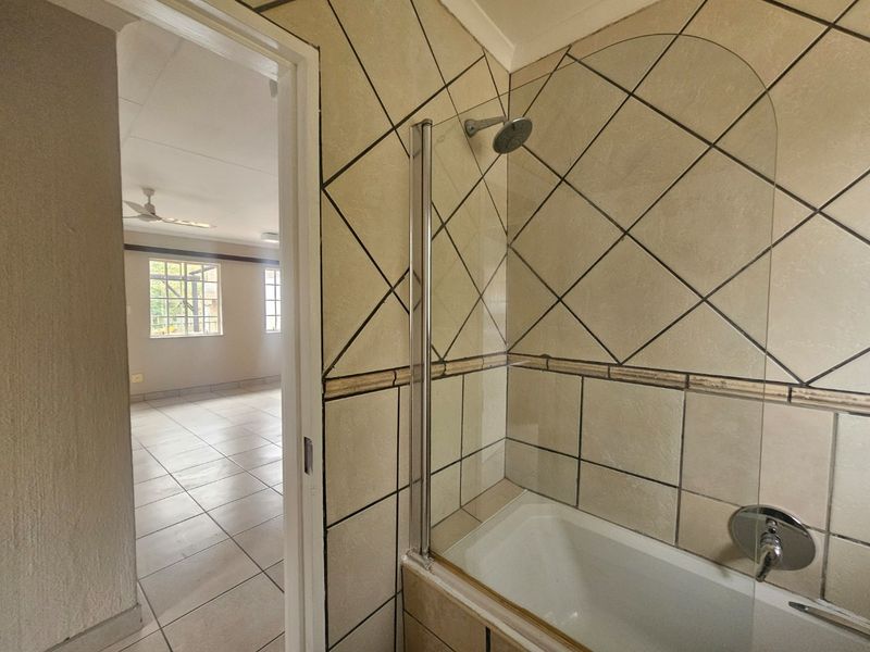 A functional bathroom featuring a bathtub with a glass shower screen and tiled finishes, adjacent to an open-plan living area.