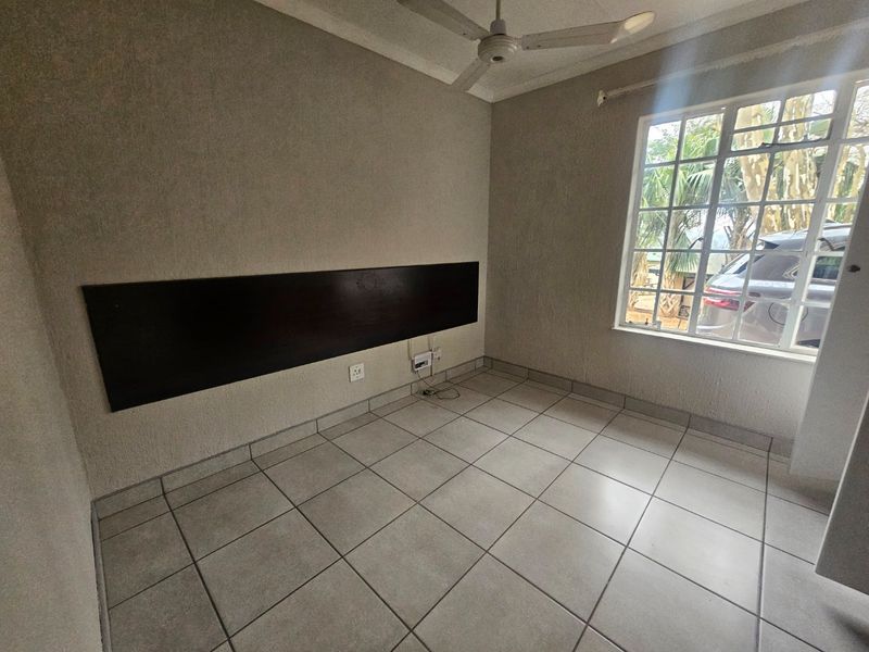 An empty bedroom featuring tiled flooring, a ceiling fan, and a built-in dark wood headboard, offering a clean canvas for personalization.