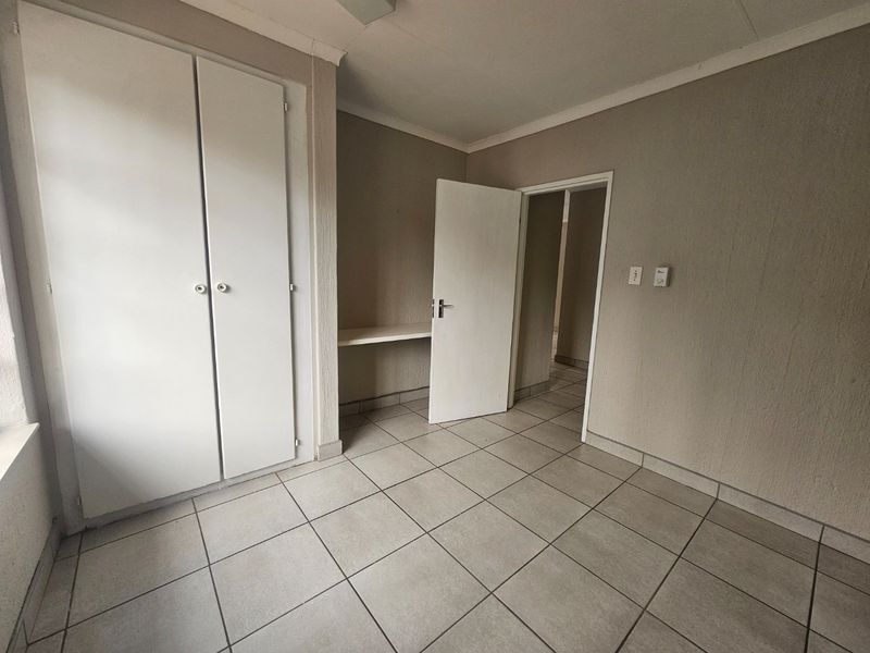 An empty bedroom featuring neutral tiled flooring, built-in cupboards, and a small built-in desk area.