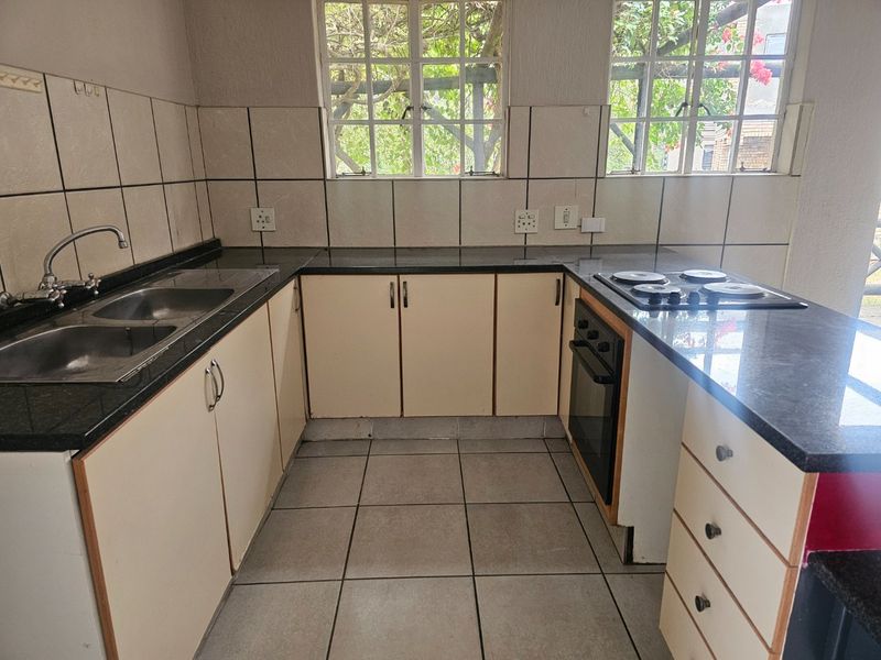 A functional kitchen featuring granite countertops, built-in cabinetry, a double basin sink, and an integrated oven with an electric hob.