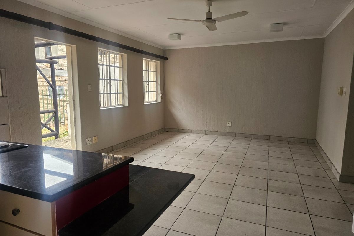 An open-plan living and kitchen area featuring tiled flooring, a ceiling fan, and a kitchen island with granite countertops, leading to an outdoor space.