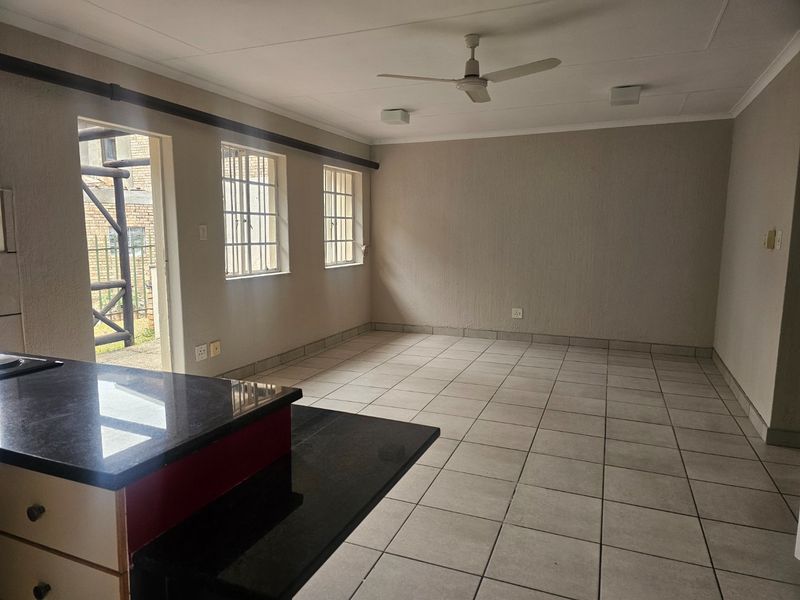 An open-plan living and kitchen area featuring tiled flooring, a ceiling fan, and a kitchen island with granite countertops, leading to an outdoor space.