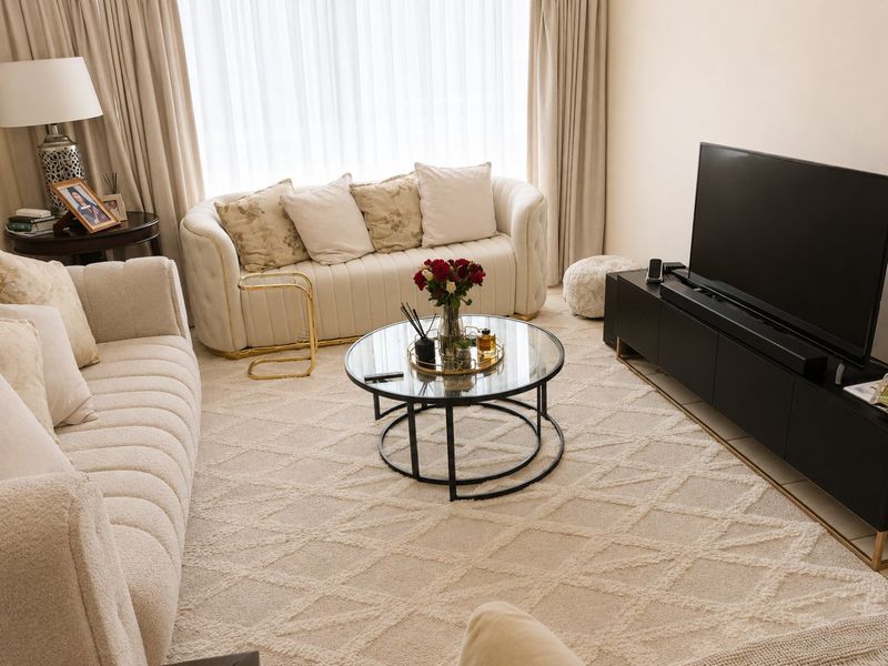 A well-maintained living room featuring neutral tones, large windows with floor-to-ceiling curtains, and tiled flooring.