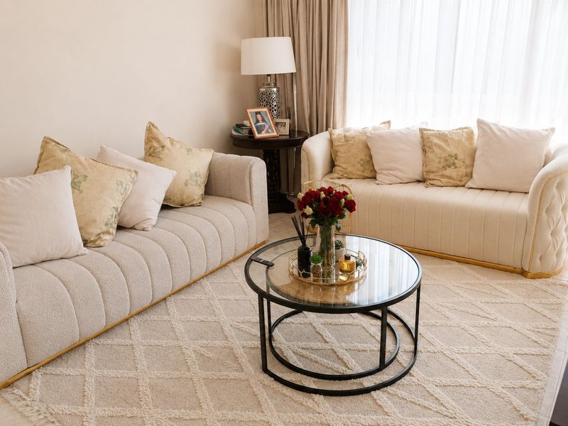 A well-lit living room area featuring neutral tones, soft textures, and large windows with floor-to-ceiling curtains.