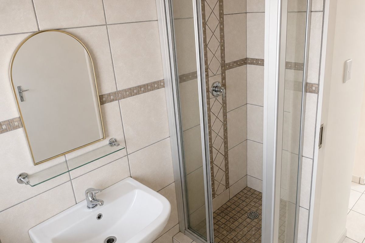 A clean, functional bathroom featuring a tiled shower enclosure, a wall-mounted basin with a mixer tap, and neutral wall tiling.