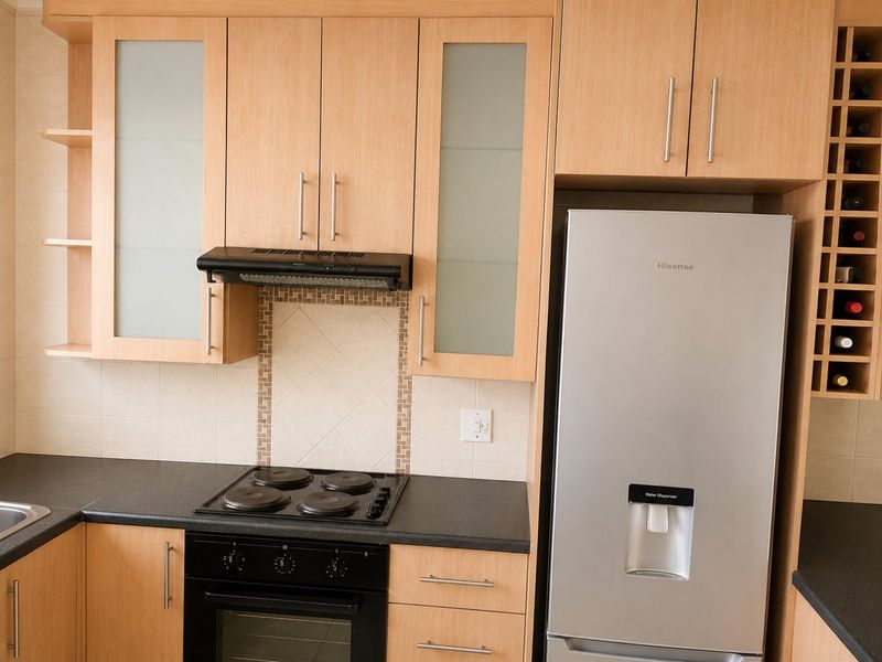 A functional kitchen featuring light wood cabinetry, dark laminate countertops, a built-in electric oven and hob, and a dedicated wine storage rack.