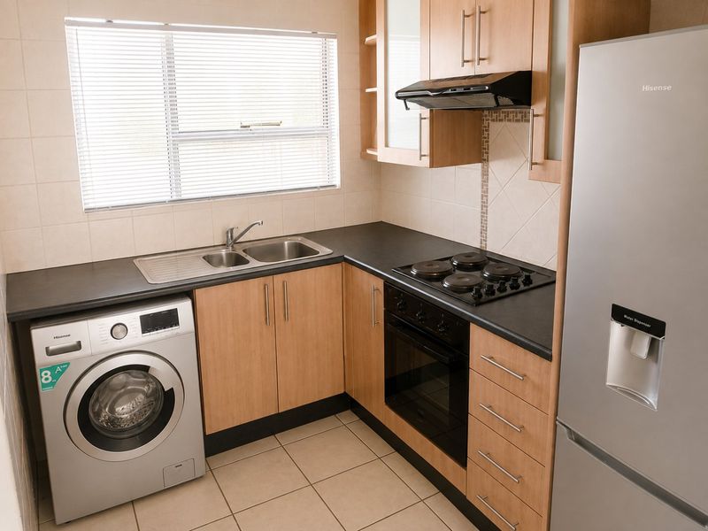 Compact kitchen featuring light wood cabinetry, dark laminate countertops, built-in oven with hob, extractor fan, and integrated space for a washing machine.