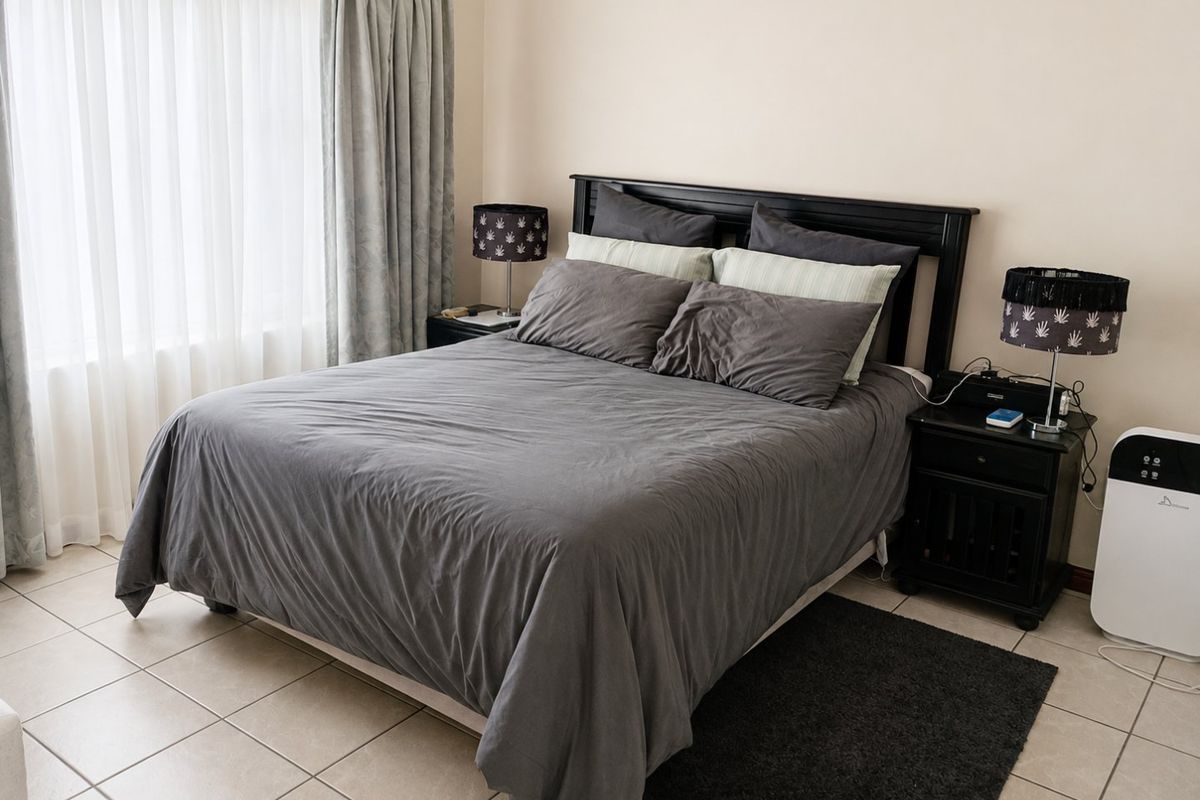 A functional bedroom featuring neutral tiled flooring and large windows with installed curtain tracks, providing a clean and simple living space.
