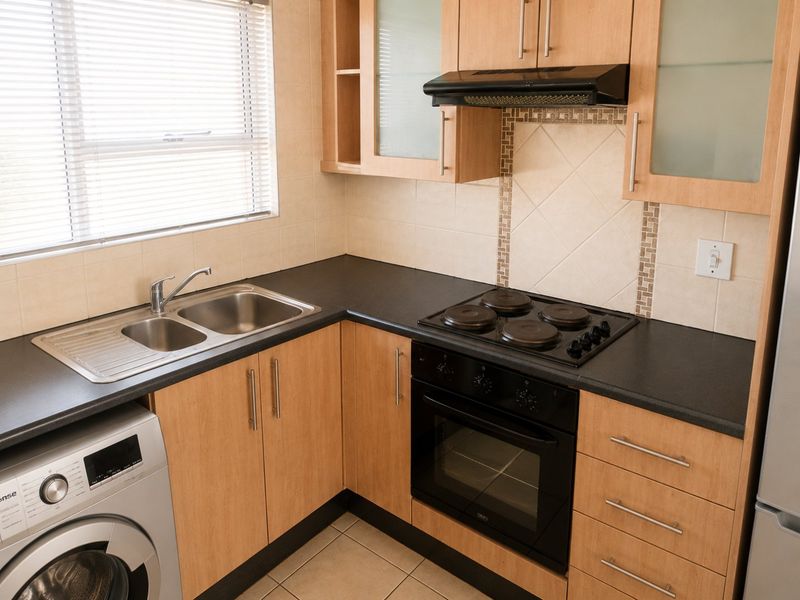 A functional kitchen featuring light wood-finish cabinetry, dark laminate countertops, a built-in oven with hob, and a stainless steel double sink.