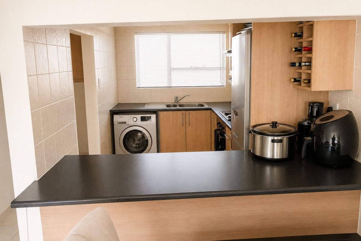 Functional kitchen featuring light wood cabinetry, dark countertops, integrated washing machine, and a convenient breakfast bar pass-through to the living area.