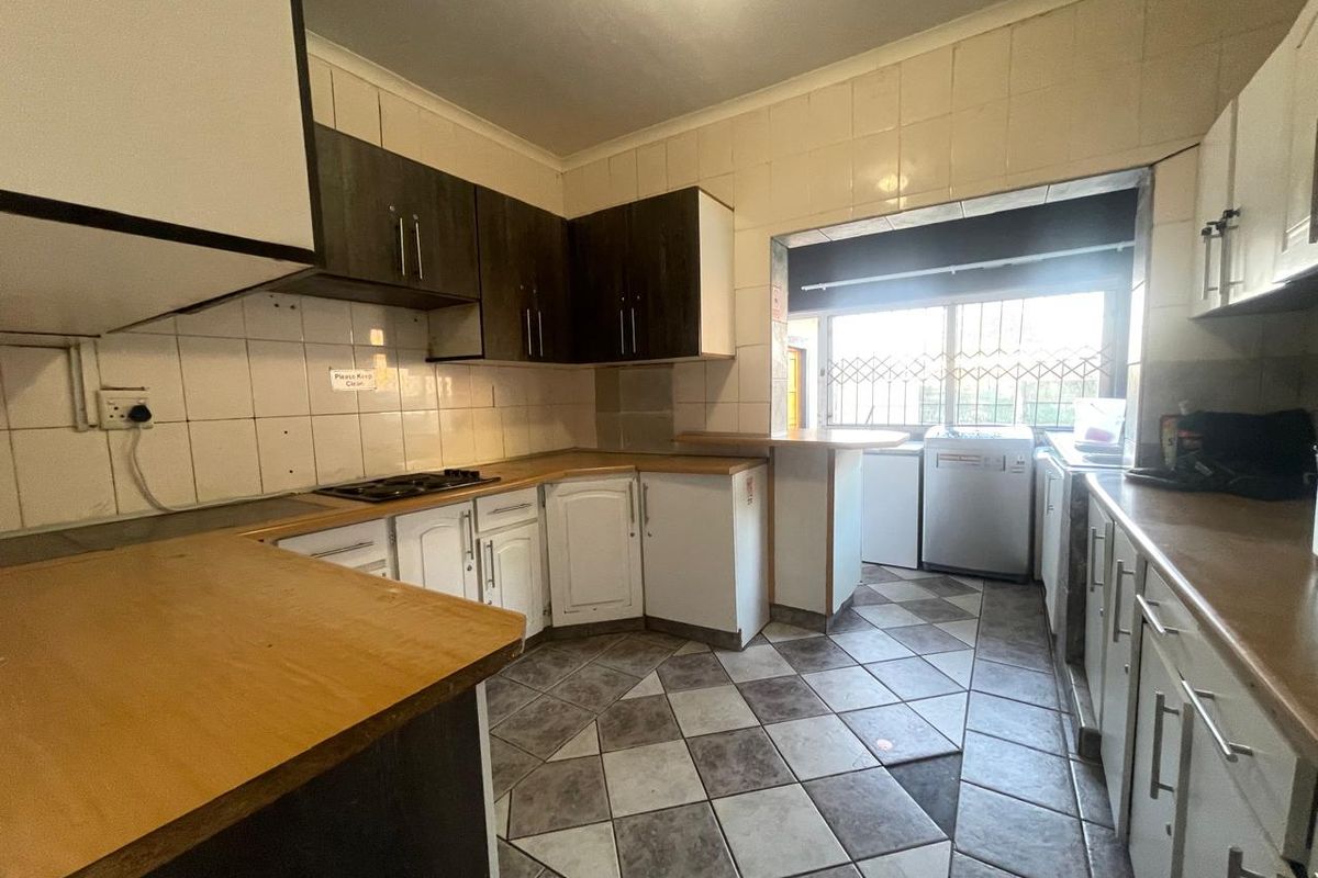 A functional kitchen featuring built-in cabinetry, laminate countertops, a hob, and tiled flooring, offering a practical layout with a breakfast bar area.