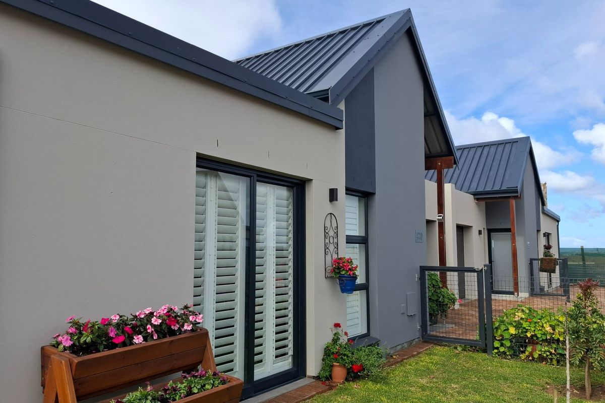 Modern rear exterior view of the house featuring a metal roof, sliding glass doors with shutters, and a landscaped garden area.