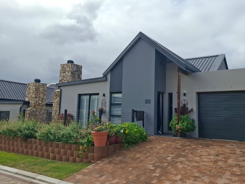 Modern single-story residence featuring a stone chimney, metal roof, paved driveway, and integrated garage, set within a well-maintained landscaped front garden.