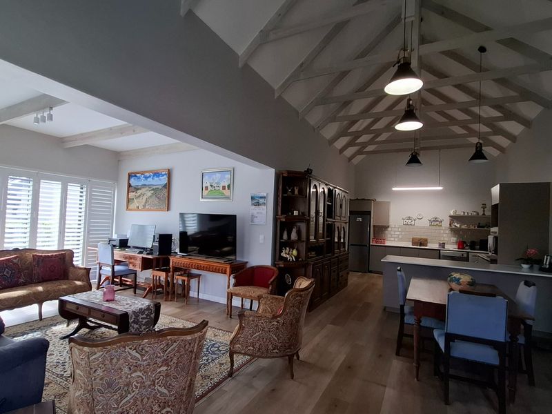 Spacious open-plan living and kitchen area featuring a striking vaulted ceiling with exposed timber trusses, modern laminate flooring, and a functional kitchen island.