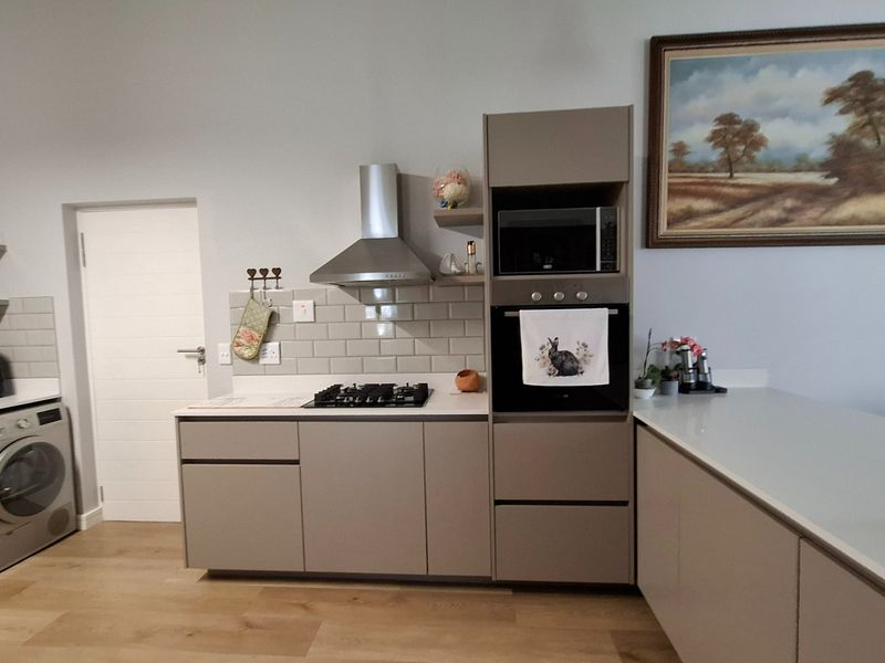 Modern kitchen featuring sleek cabinetry, subway tile backsplash, built-in oven, microwave, and gas hob with integrated laundry appliances.