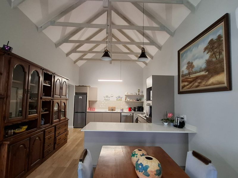 Spacious open-plan kitchen and dining area featuring high vaulted ceilings with exposed timber trusses, modern cabinetry, and a central island bench.