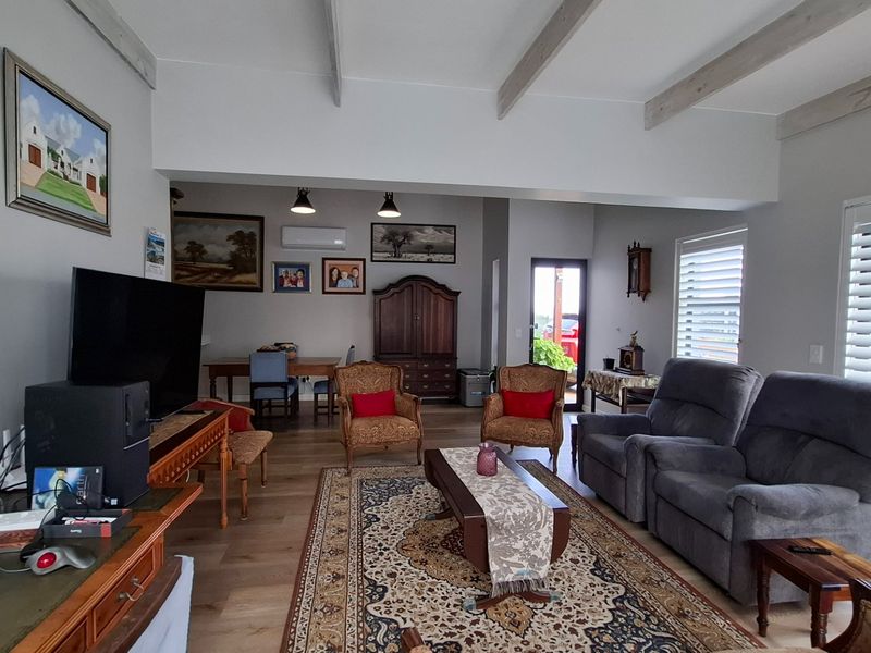 Spacious open-plan living area featuring exposed ceiling beams, laminate flooring, plantation shutters, and direct access to the outdoors through French doors.