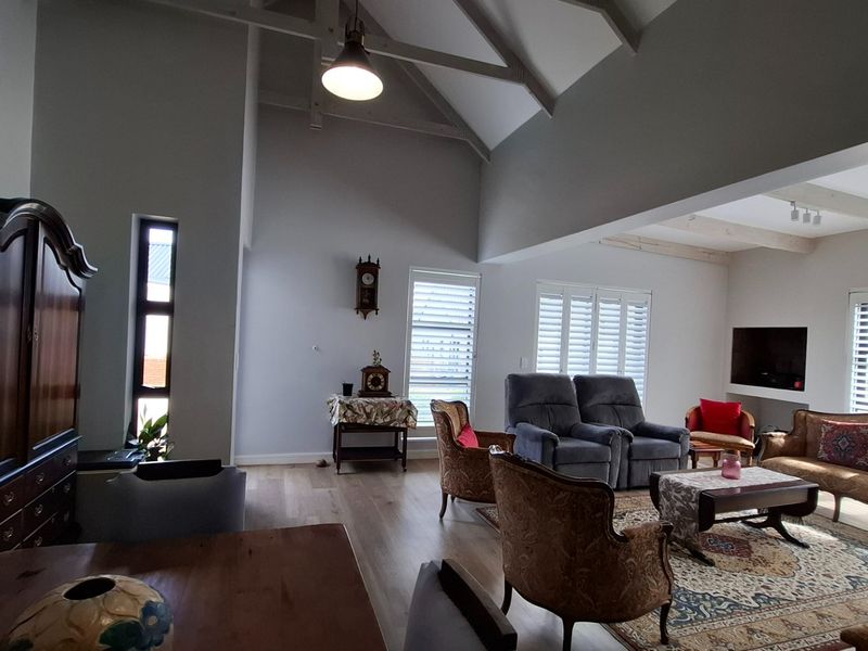 Spacious living room featuring high vaulted ceilings with exposed rafters, timber flooring, and plantation shutters, creating a bright and airy atmosphere.
