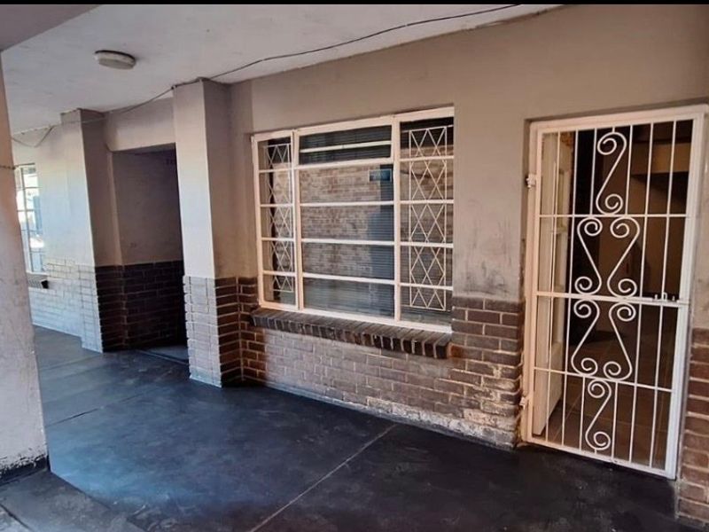 Exterior view of an apartment entrance featuring a covered walkway, brick facade, and security gate.
