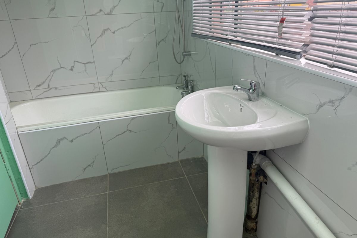 A functional bathroom featuring a pedestal basin, bathtub with shower mixer, and modern marble-look wall tiling.
