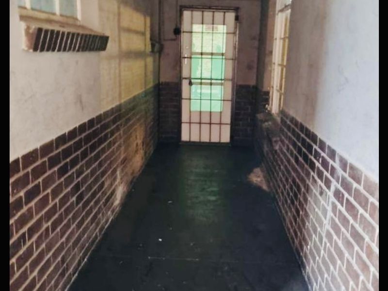 A narrow hallway featuring brick wainscoting, a security gate, and casement windows, currently in need of cosmetic refurbishment and surface repairs.