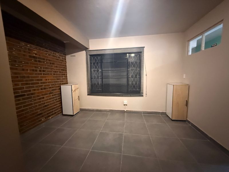 A clean, empty bedroom featuring a rustic exposed brick wall, large format floor tiles, and built-in storage units.