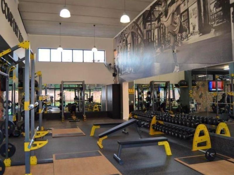 A well-equipped fitness facility featuring mirrored walls, durable rubberized flooring, and high ceilings with integrated lighting.
