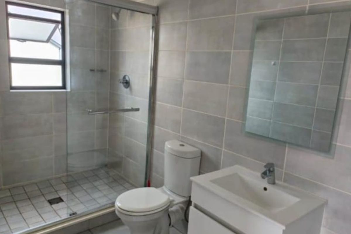 A clean, modern bathroom featuring a glass-enclosed shower, a vanity basin with storage, and neutral wall and floor tiling.