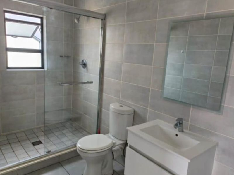 A clean, modern bathroom featuring a glass-enclosed shower, a vanity basin with storage, and neutral wall and floor tiling.