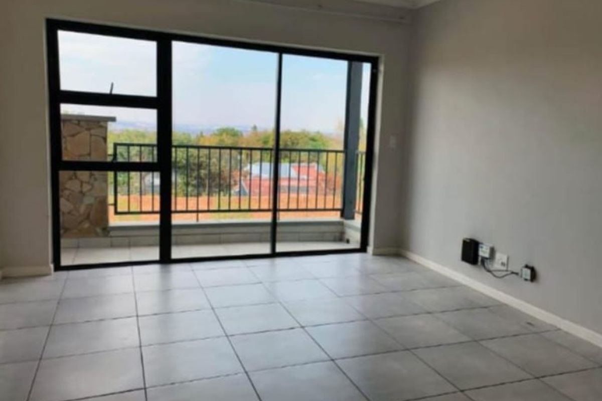 A bright, empty living room featuring neutral tiled flooring and large sliding glass doors that open onto a balcony with scenic views.